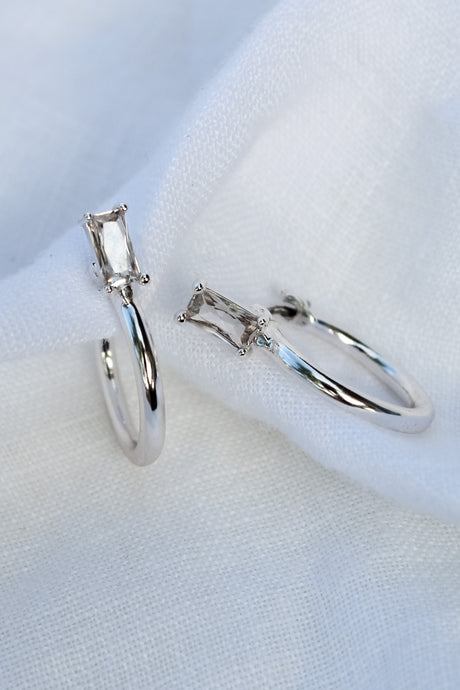 The Darra Mini Silver rings by Kinsey Designs Archives, crafted from rhodium plated brass with rectangular clear cubic zirconia, are displayed on white fabric.