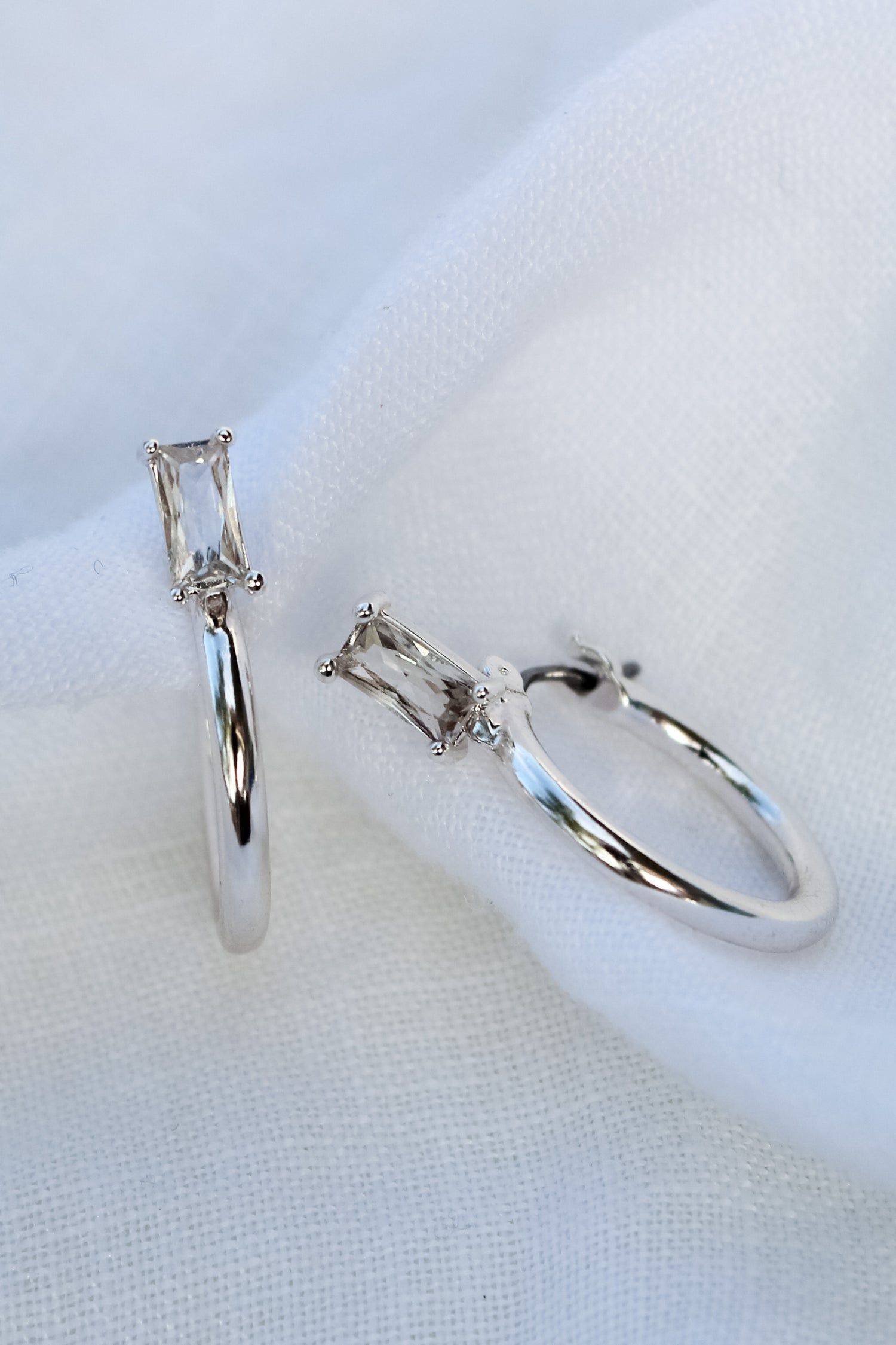 The Darra Mini Silver hoop earrings by Kinsey Designs Archives feature rectangular Cubic Zirconia, crafted from rhodium-plated brass, measure 3/4" in diameter, and are elegantly displayed on white fabric.