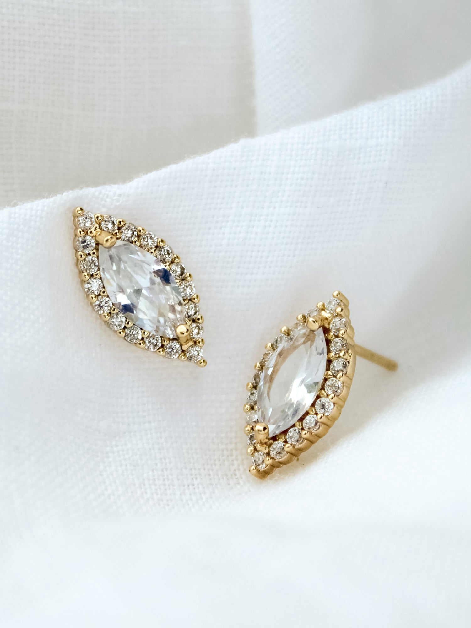 The Dina Post by Kinsey Designs Archives features gold filled marquise-shaped stud earrings with cubic zirconia and a halo of small diamonds, beautifully displayed on white fabric.