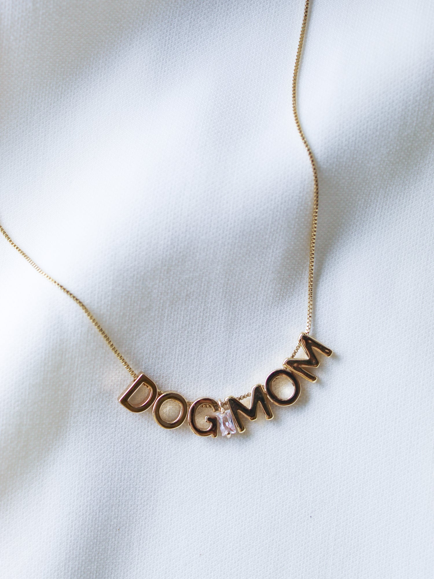 Kinsey Designs Archives Dog Mom Slide Necklace shown on white fabric, features gold-filled chain, adjustable Italian closure, and letter charms spelling "DOG MOM.