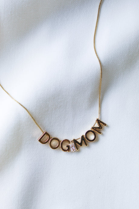 Kinsey Designs Archives Dog Mom Slide Necklace shown on white fabric, features gold-filled chain, adjustable Italian closure, and letter charms spelling "DOG MOM.