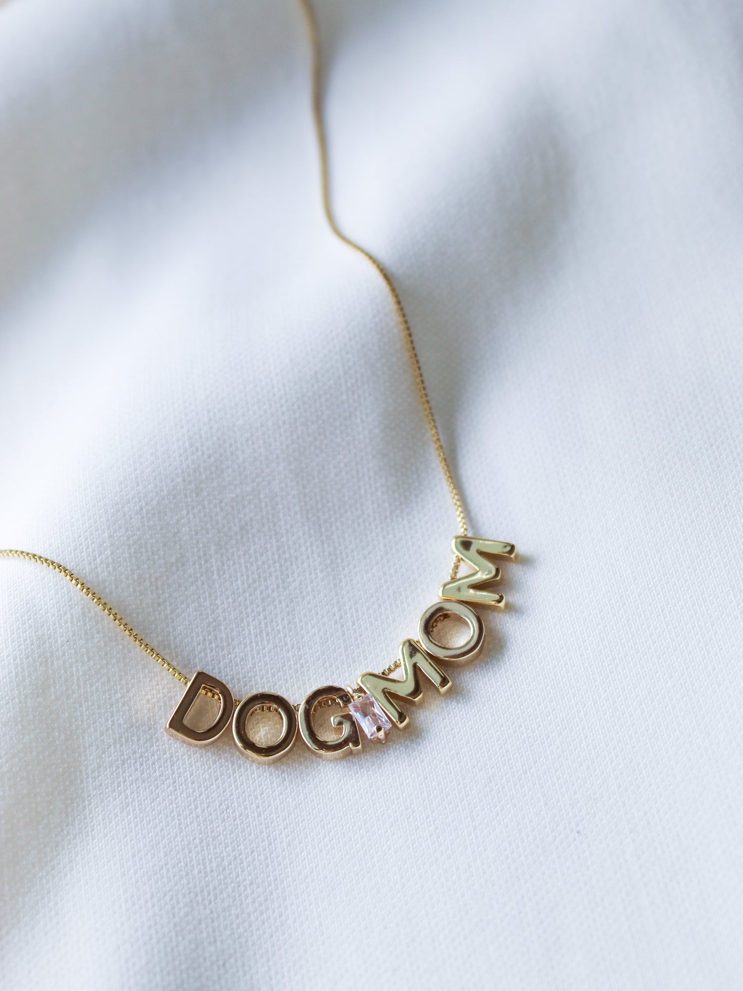Dog Mom Slide Necklace by Kinsey Designs Archives shown on white fabric, featuring “DOG MOM” gold letter charms on an 18" gold filled chain with adjustable Italian closure.