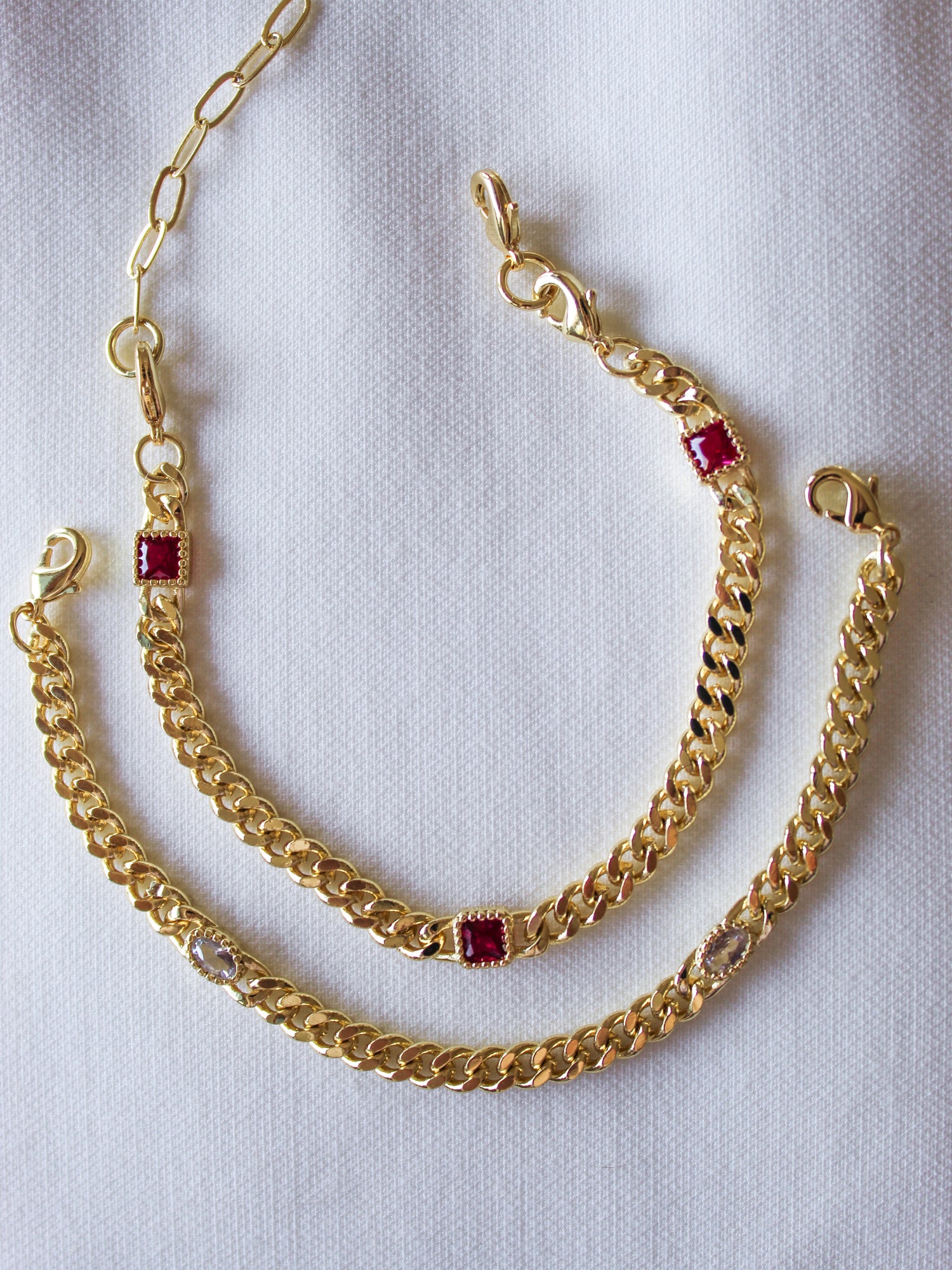 The Kinsey Designs Dublin Bracelet (3 in 1), featuring gold-filled chains with gemstone and cubic zirconia accents, rests on a white fabric background.
