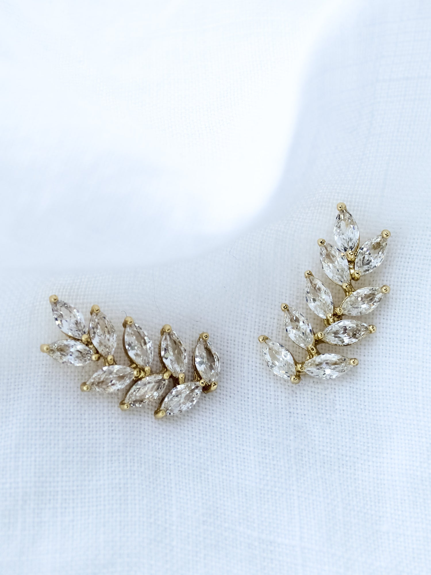 The Elio Climber by Kinsey Designs Archives features leaf-shaped clear gemstones in a curved design—chic earrings perfect for a stylish sample sale find, beautifully displayed on white fabric.