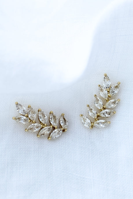 The Elio Climber by Kinsey Designs Archives features leaf-shaped clear gemstones in a curved design—chic earrings perfect for a stylish sample sale find, beautifully displayed on white fabric.