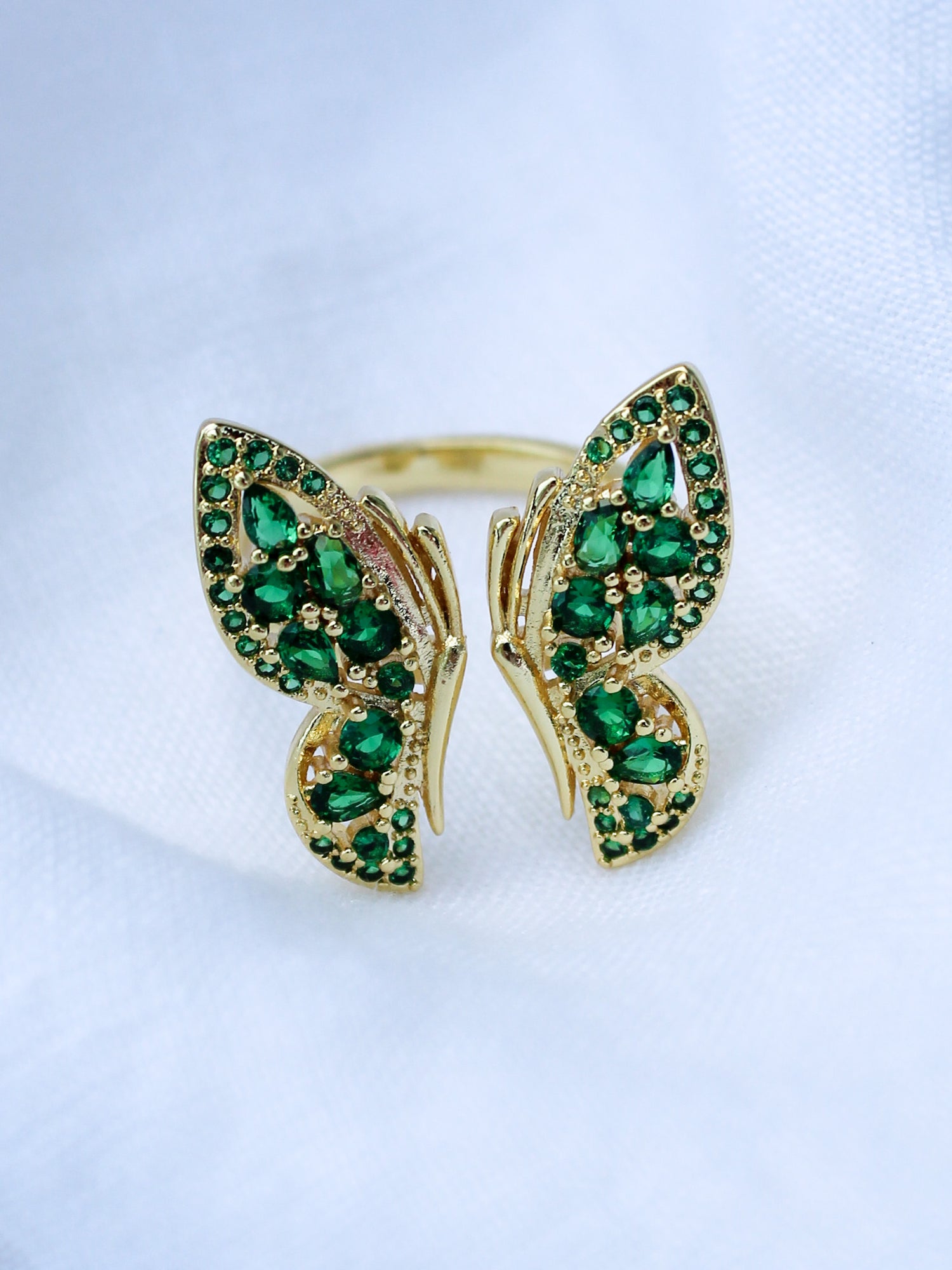 The Ezra Ring by Kinsey Designs Archives features a gold-filled butterfly shape with a .75" face, set with green gemstones and shown on a white fabric background.