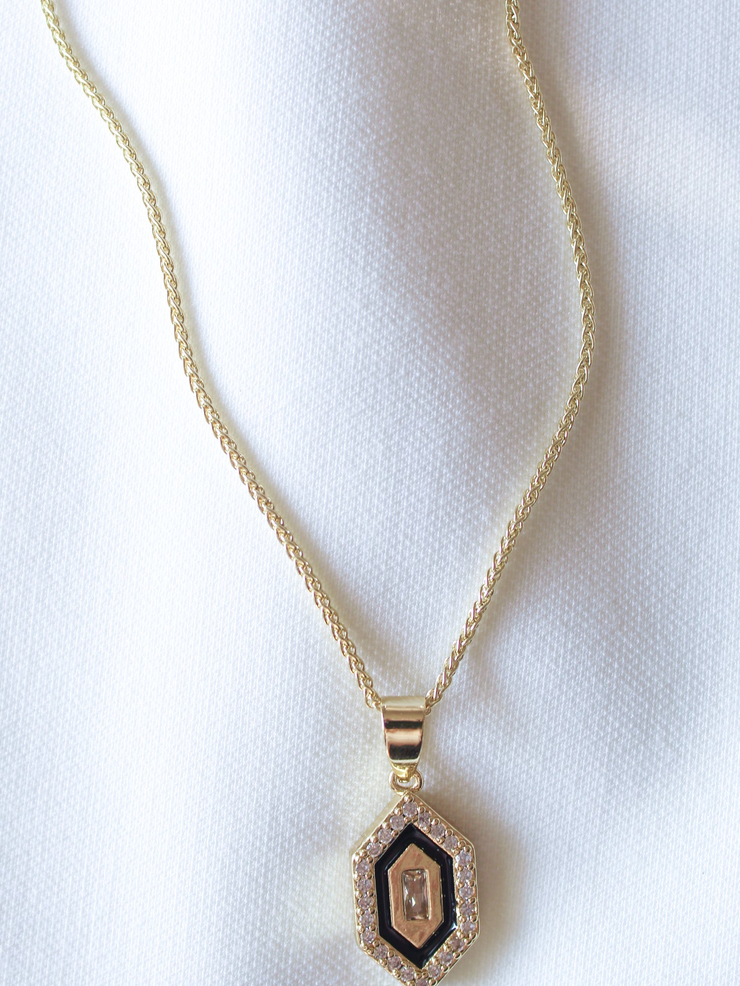 The Harlowe Necklace by Kinsey Designs Archives features a gold filled chain (17.75 in) with a hexagon cubic zirconia pendant accented with diamonds, displayed on textured white fabric for an elegant look.