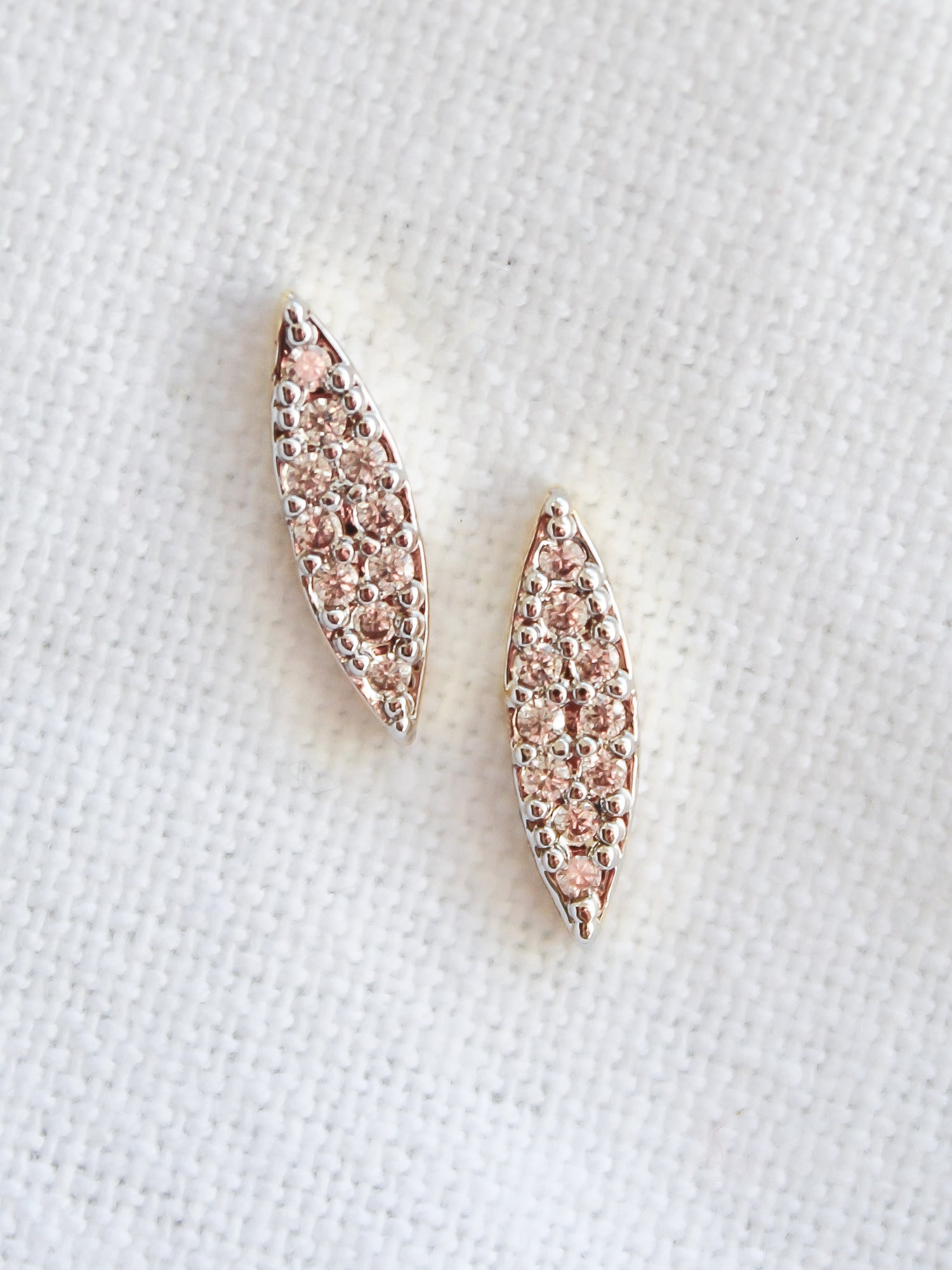 The Her Post earrings by Kinsey Designs Archives feature two marquise-shaped, 16k rose gold filled pieces adorned with sparkling cubic zirconia, displayed on a white textured background.