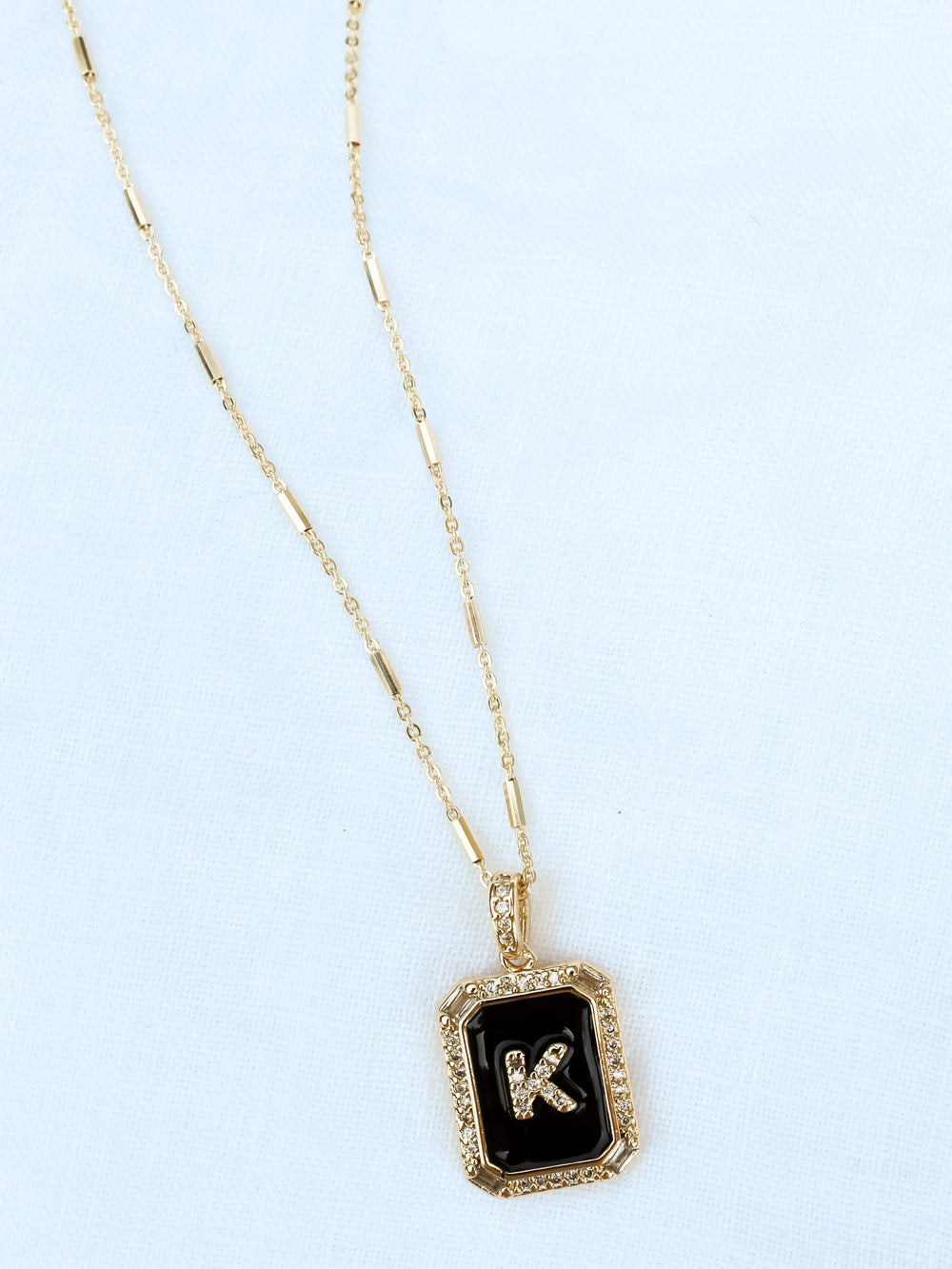 The Initial Tile Necklace Ink by Kinsey Designs Archives features a black pendant with the letter "K" on a white textured background—an elegant piece of monogram jewelry and a stylish personalized necklace.