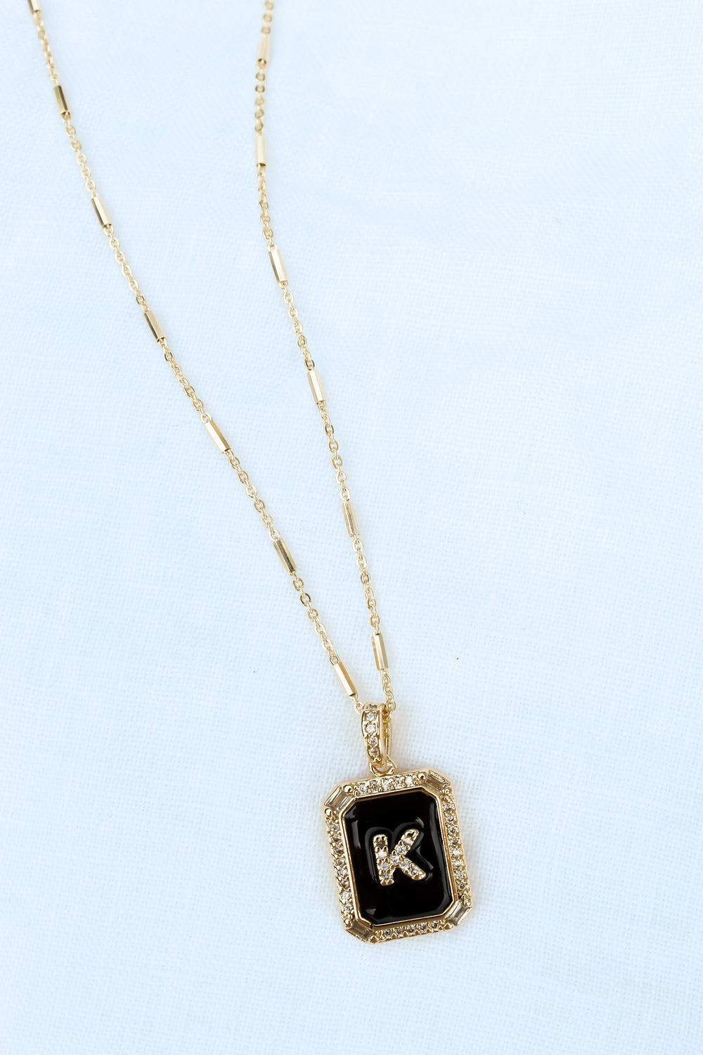 The Initial Tile Necklace Ink by Kinsey Designs Archives features a black pendant with the letter "K" on a white textured background—an elegant piece of monogram jewelry and a stylish personalized necklace.
