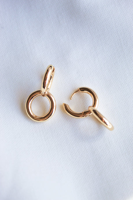 Two small Interlock Huggie earrings by Kinsey Designs Archives in 14k gold plated brass rest on a white fabric background—one closed, one slightly open—a perfect sample sale find.