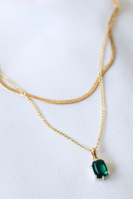 The Kelley Layer by Kinsey Designs Archives features an 18" gold plated chain with a bold green gemstone pendant, elegantly showcased on a white fabric background.