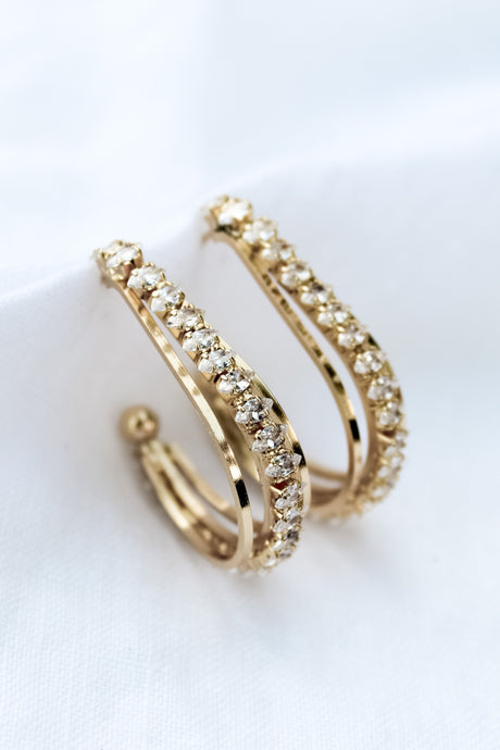 The Kenny Earring by Kinsey Designs Archives features gold-filled hoops adorned with two rows of sparkling cubic zirconia, displayed on a white fabric background.