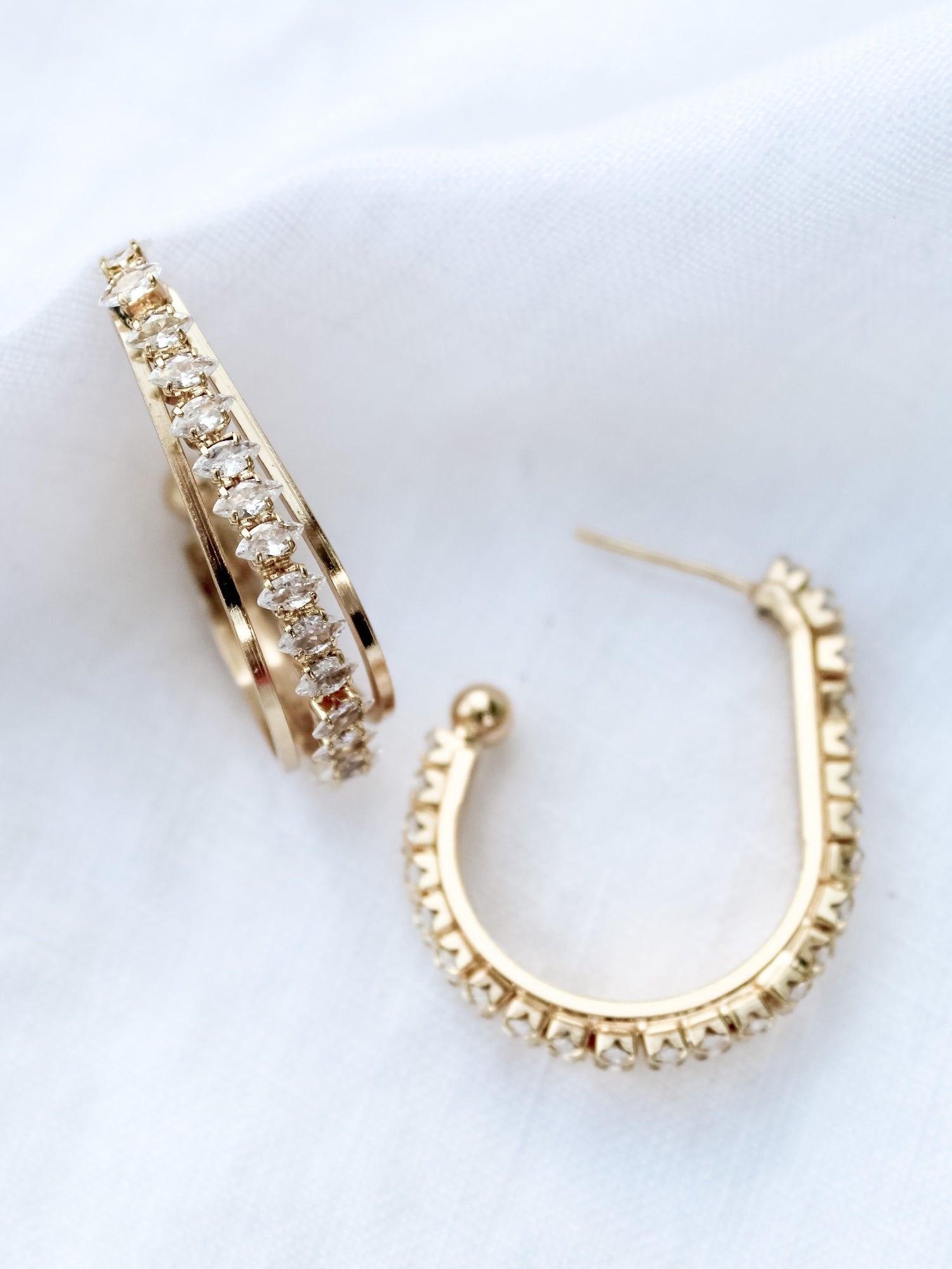 The Kenny Earring by Kinsey Designs Archives features gold-filled hoops with embedded cubic zirconia, adding subtle sparkle to your jewelry collection. Shown against a white fabric background.