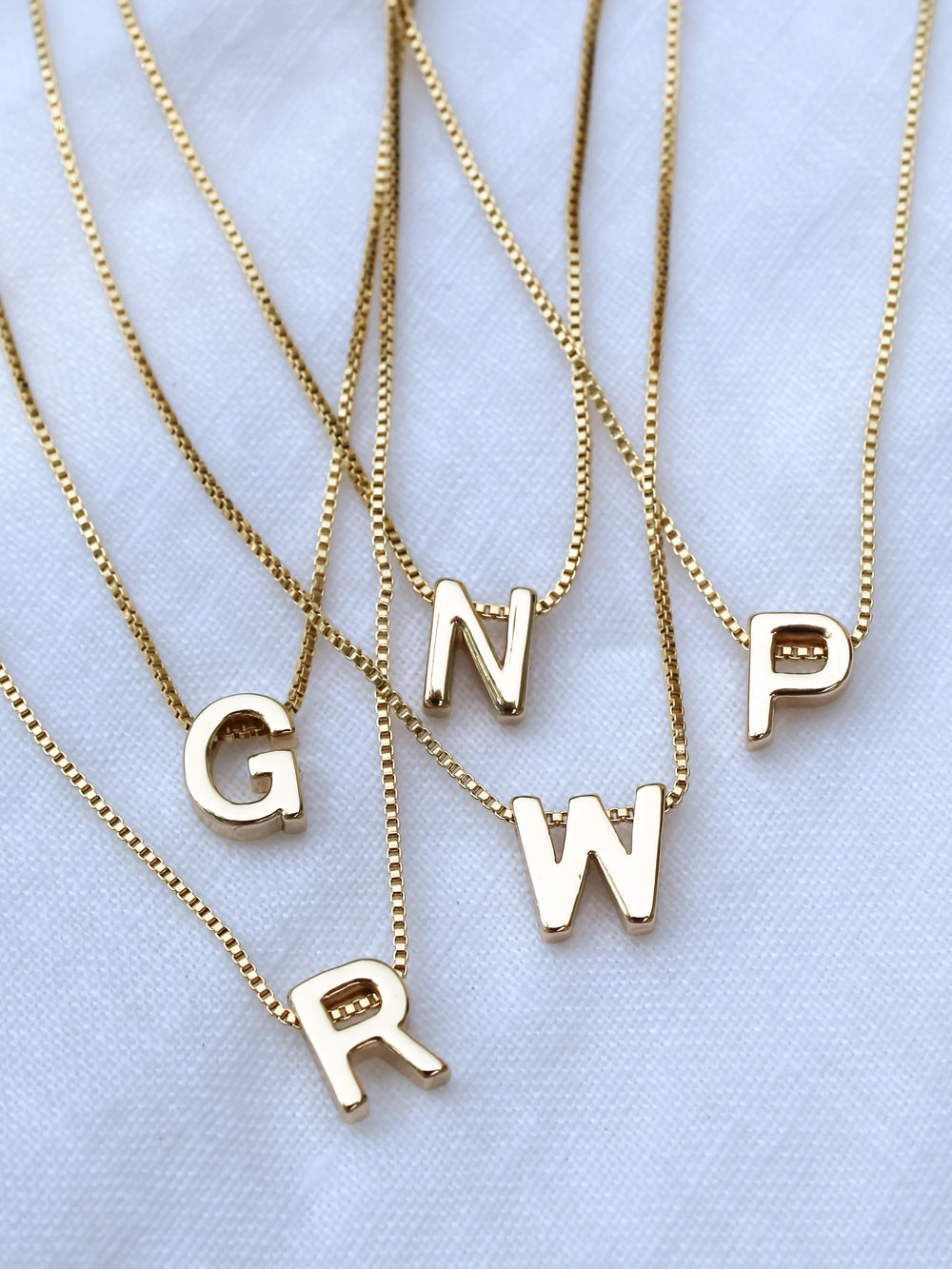 Five Kinsey Designs Collection gold necklaces featuring the Kinsey Slide Initial Necklace Letter A displayed on a white fabric background.