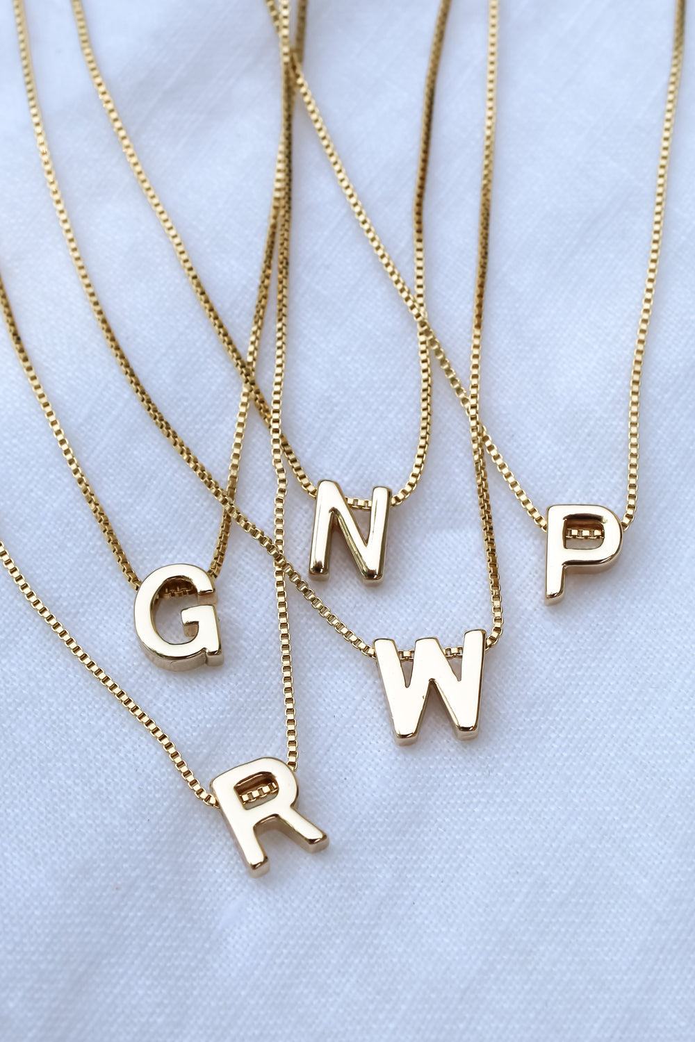 Five Kinsey Designs Collection gold necklaces featuring the Kinsey Slide Initial Necklace Letter A displayed on a white fabric background.