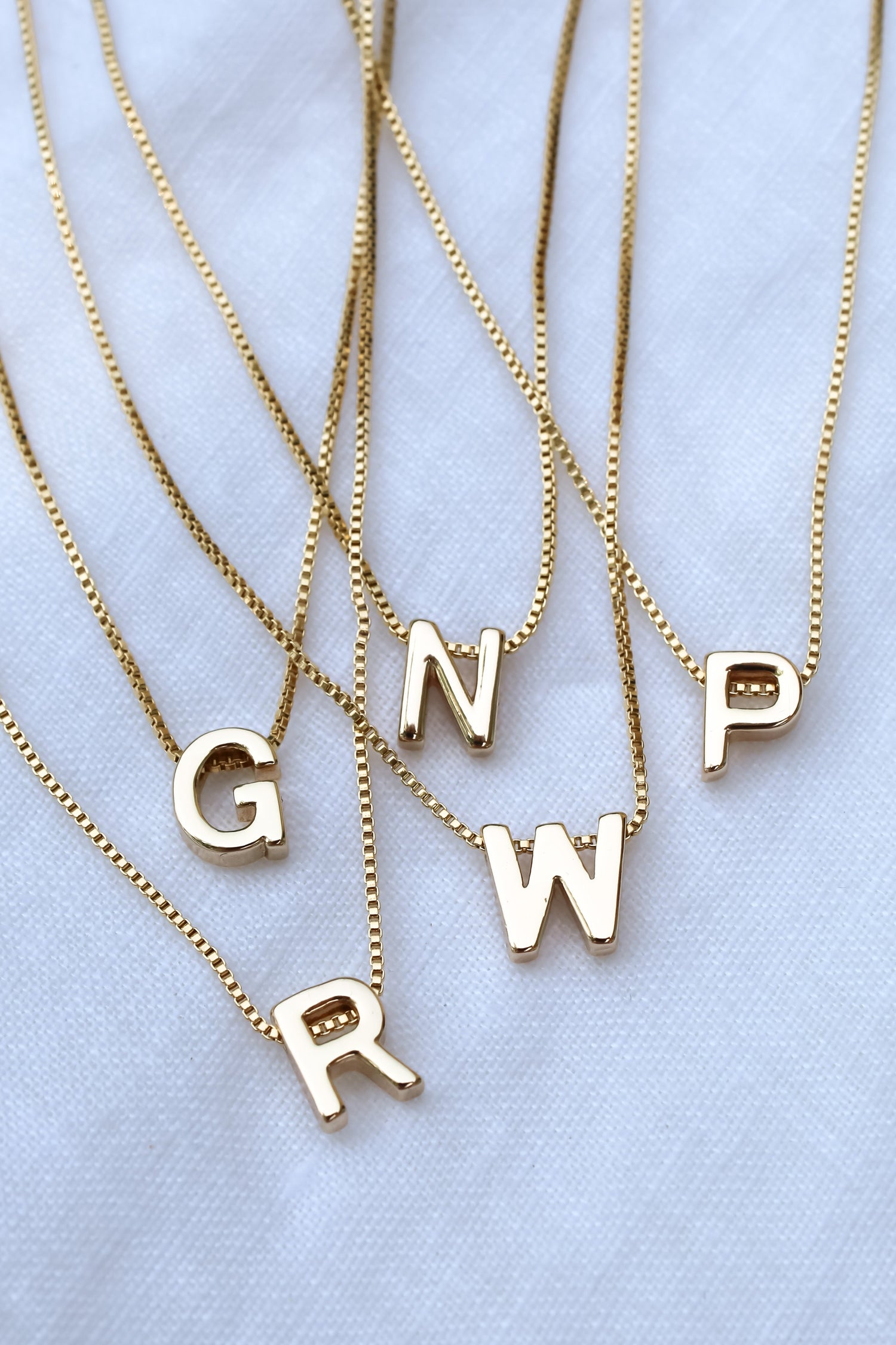 Five Kinsey Designs Collection gold necklaces featuring the Kinsey Slide Initial Necklace Letter A displayed on a white fabric background.