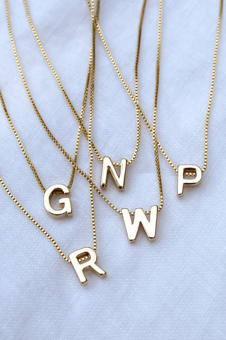 Five Kinsey Designs Collection gold necklaces featuring the Kinsey Slide Initial Necklace Letter A displayed on a white fabric background.