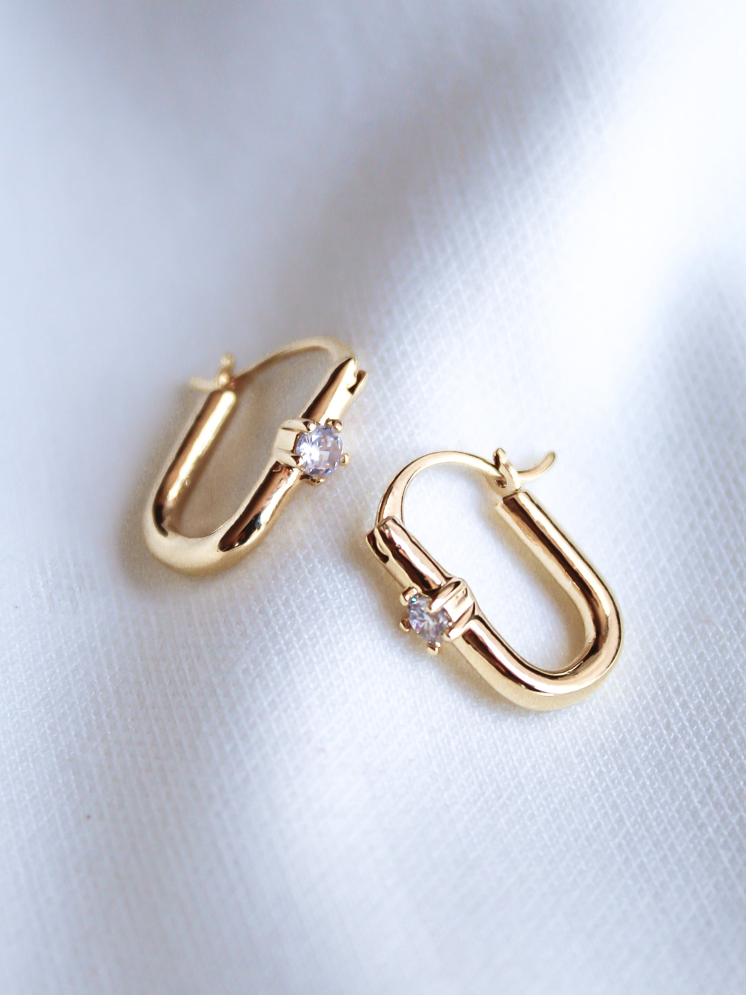 The Lou Hoop by Kinsey Designs Archives features 14k gold plating and sparkling cubic zirconia, elegantly displayed on white fabric.