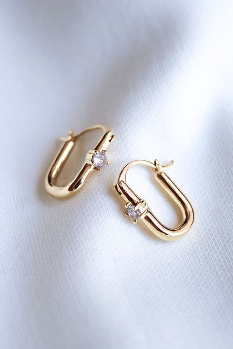 The Lou Hoop by Kinsey Designs Archives features 14k gold plating and sparkling cubic zirconia, elegantly displayed on white fabric.
