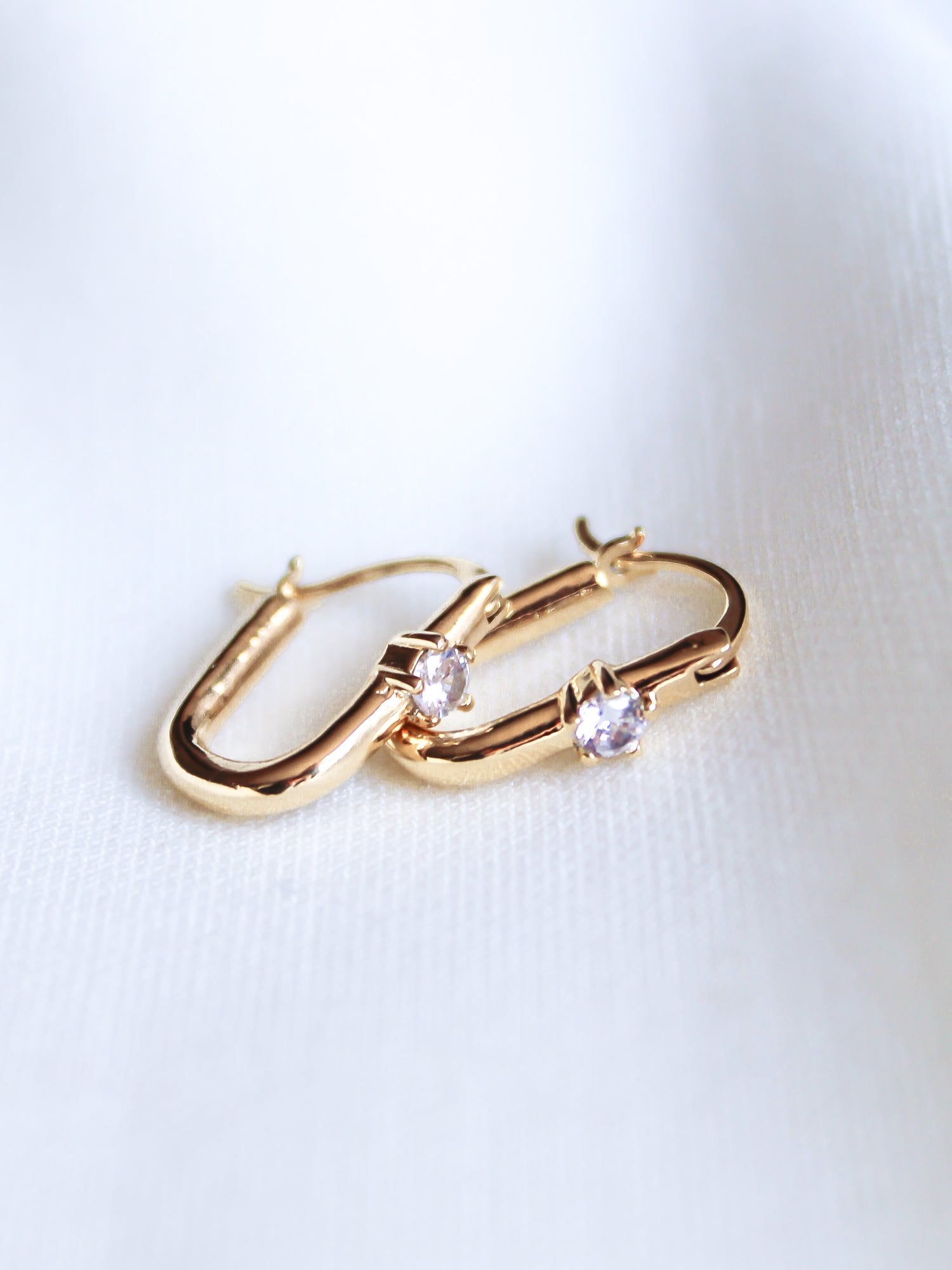 The Lou Hoop by Kinsey Designs Archives features 14k gold plating and small round cubic zirconia stones, displayed on a soft white fabric background.