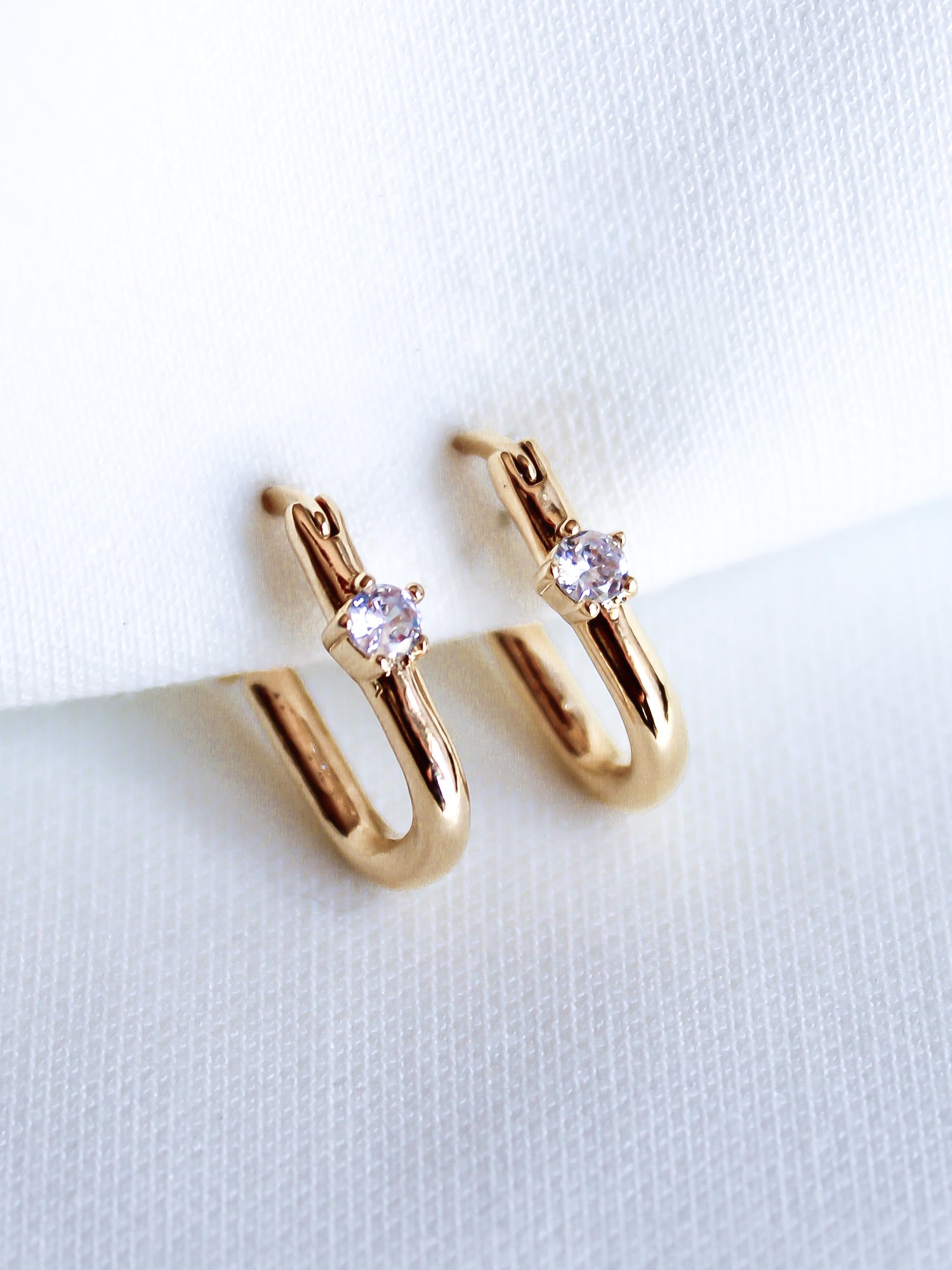 The Lou Hoop by Kinsey Designs Archives features 14k gold plating and small clear cubic zirconia stones, elegantly presented on white fabric.