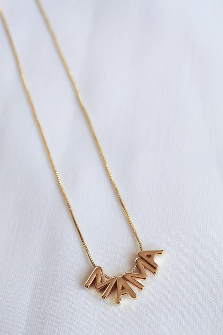 The MAMA Slide Necklace by Kinsey Designs Archives features gold letter charms spelling "MAMA" on a white fabric background, with a 14k gold filled 18" chain and an adjustable Italian closure.