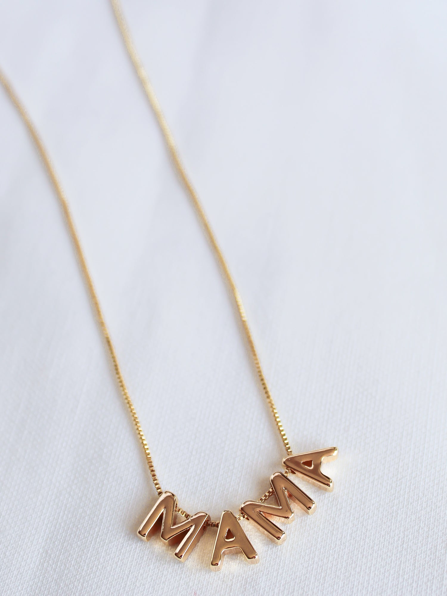 The MAMA Slide Necklace by Kinsey Designs Archives features pendant letters spelling "MAMA" on a white fabric background, an adjustable Italian closure, and is crafted in 14k gold filled on an elegant 18" chain.