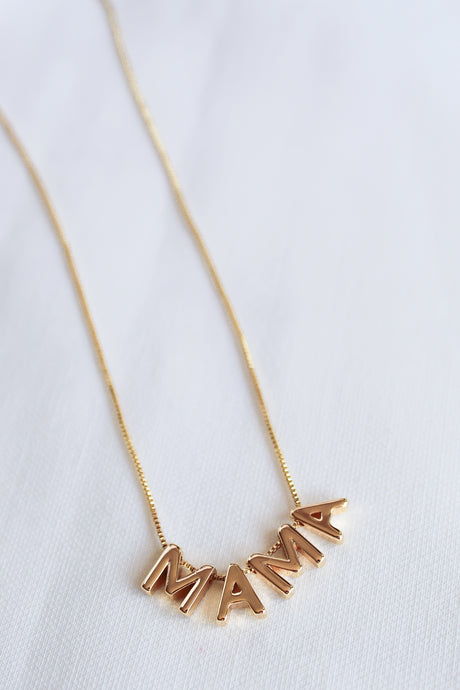 The MAMA Slide Necklace by Kinsey Designs Archives features pendant letters spelling "MAMA" on a white fabric background, an adjustable Italian closure, and is crafted in 14k gold filled on an elegant 18" chain.