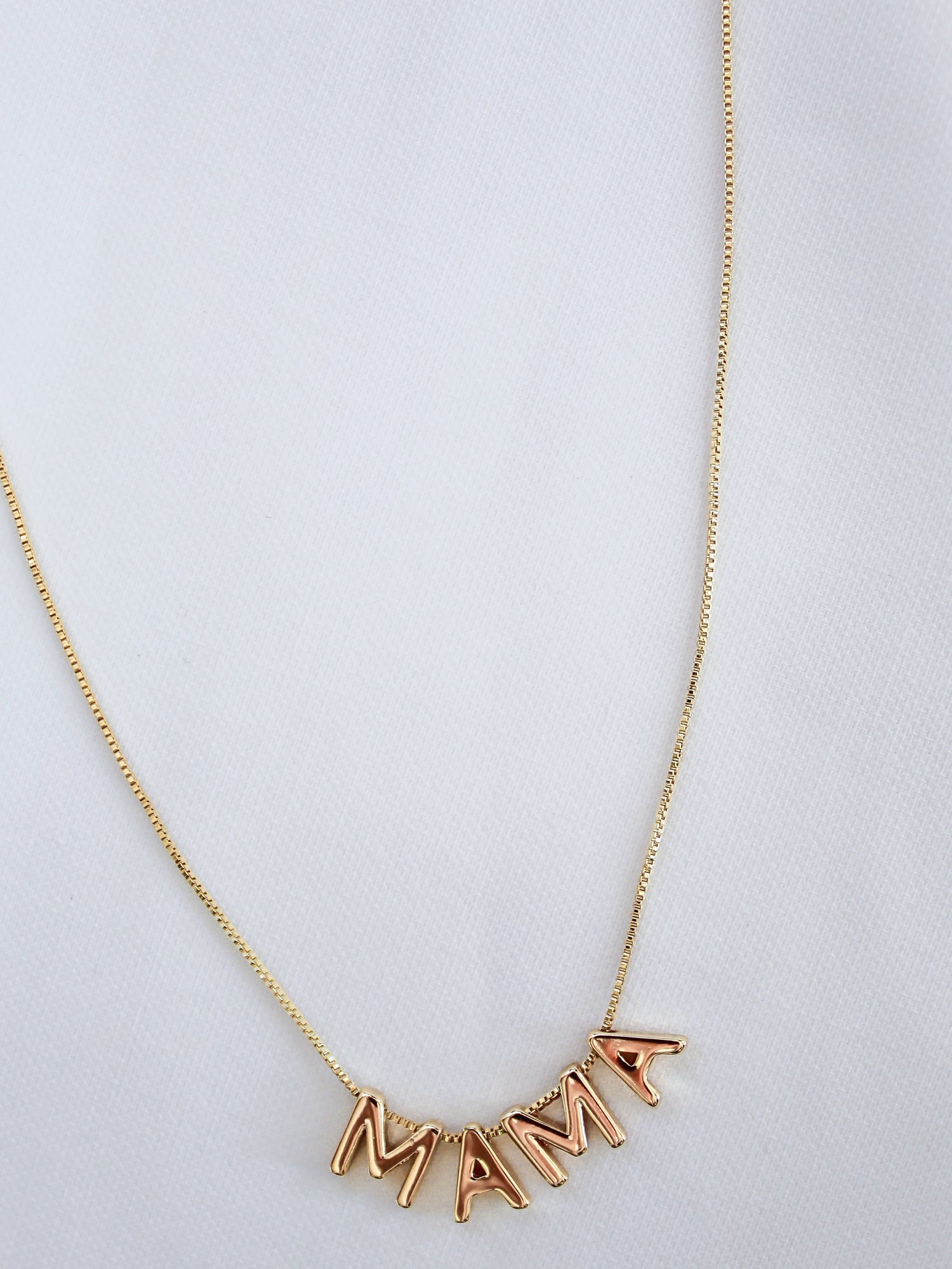 The MAMA Slide Necklace by Kinsey Designs Archives features letter charms spelling "MAMA" on a white fabric, an 18" chain, adjustable Italian closure, and radiant 14k gold filled finish.
