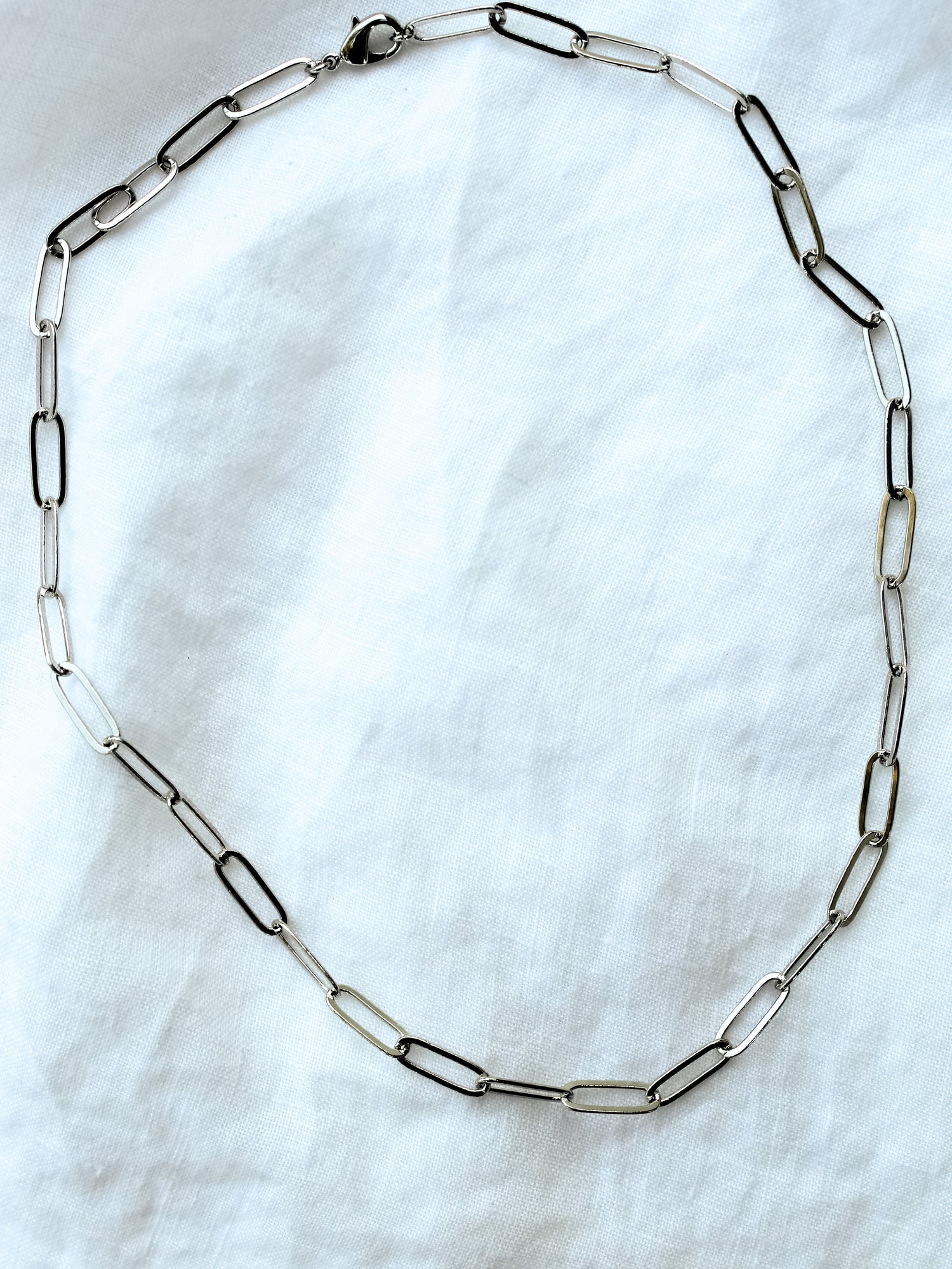 The Maeve Silver necklace by Kinsey Designs Archives features a 17" 14K gold filled paperclip chain with a lobster clasp, displayed in an oval on a white fabric background.