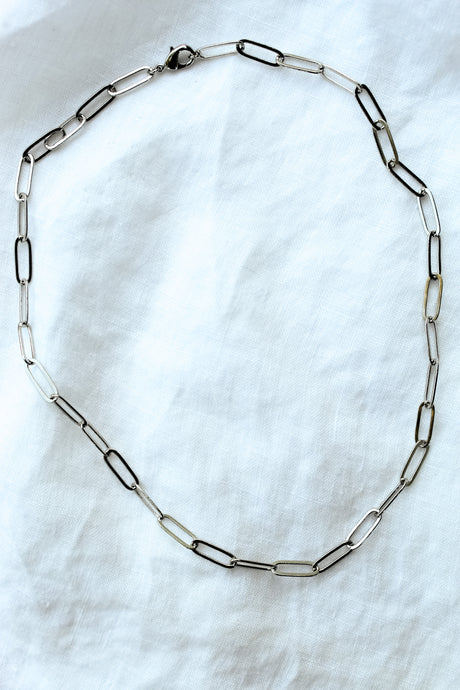 The Maeve Silver necklace by Kinsey Designs Archives features a 17" 14K gold filled paperclip chain with a lobster clasp, displayed in an oval on a white fabric background.