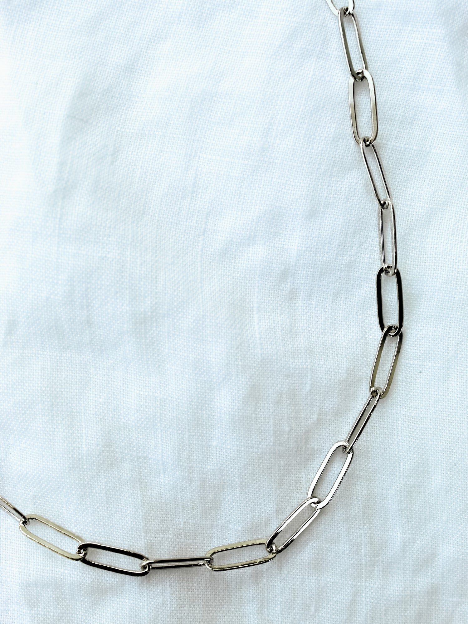 The Maeve Silver by Kinsey Designs Archives features a thin, silver chain with elongated oval links and a secure lobster clasp, displayed against a white fabric background.