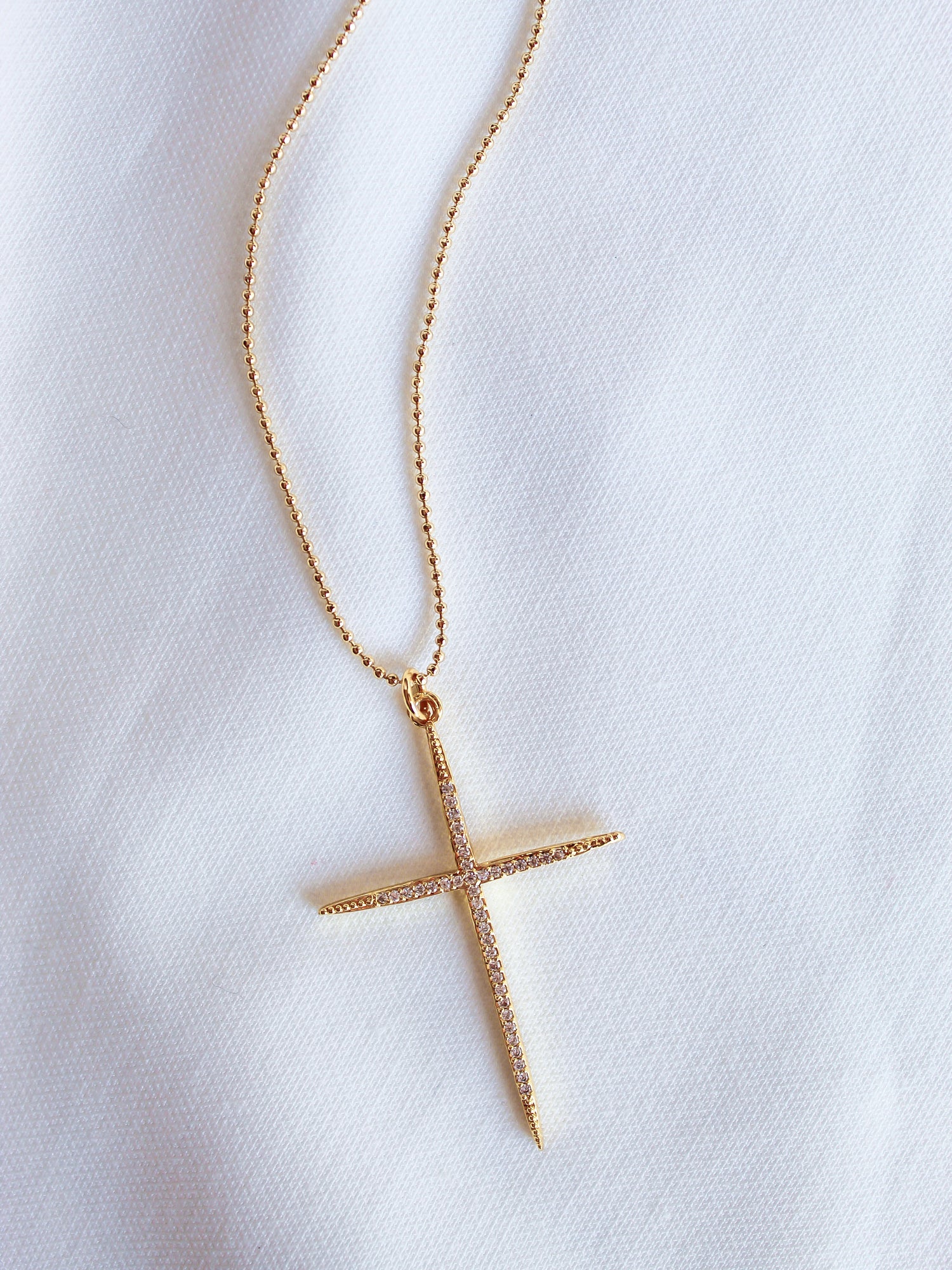 The Meyer Necklace by Kinsey Designs Archives features a gold filled cross pendant with cubic zirconia on a white fabric background. Its delicate 20-inch chain adds elegance to this stylish accessory.