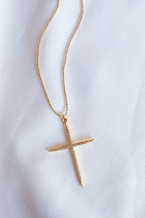 The Meyer Necklace by Kinsey Designs Archives features a gold filled cross pendant with cubic zirconia on a white fabric background. Its delicate 20-inch chain adds elegance to this stylish accessory.
