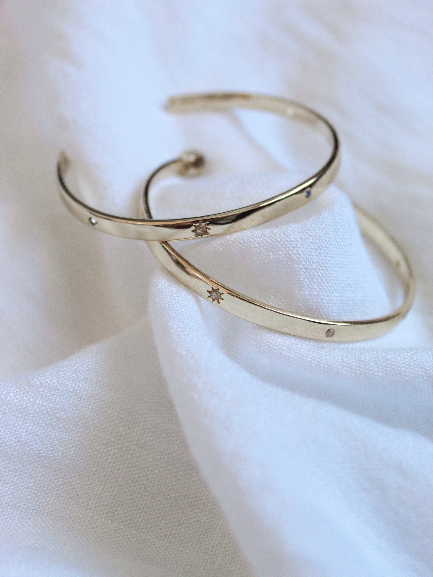 Two gold plated Molly Hoops by Kinsey Designs Archives with delicate star engravings rest on soft white fabric—a radiant duo you'll love from our exclusive Sample Sale.