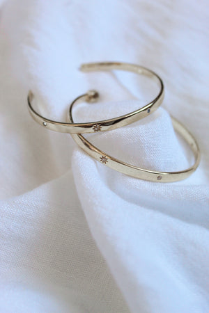 Two gold plated Molly Hoops by Kinsey Designs Archives with delicate star engravings rest on soft white fabric—a radiant duo you'll love from our exclusive Sample Sale.