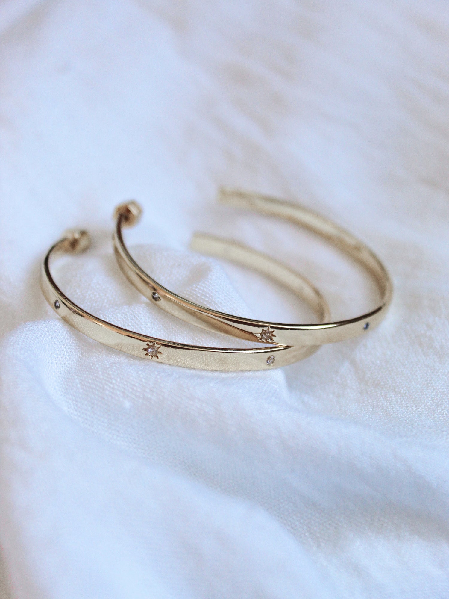 The Molly Hoop by Kinsey Designs Archives—two gold plated bangles with delicate star engravings, displayed on soft white fabric. Discover this elegant piece at our Sample Sale.