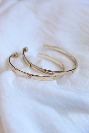 The Molly Hoop by Kinsey Designs Archives—two gold plated bangles with delicate star engravings, displayed on soft white fabric. Discover this elegant piece at our Sample Sale.