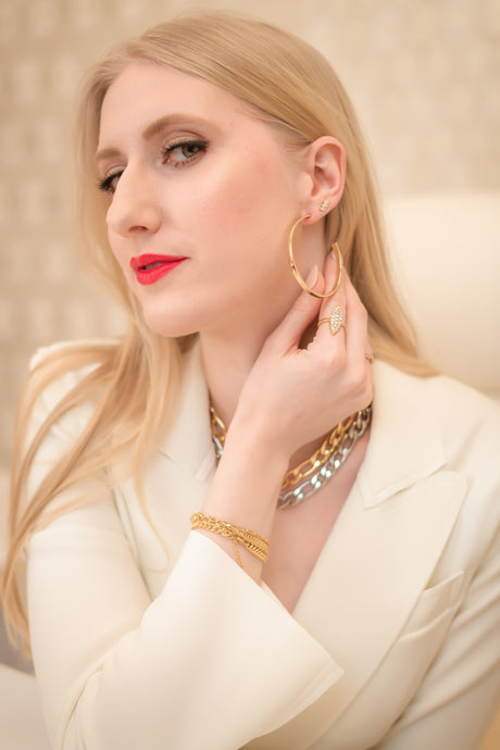 A woman with blonde hair in a white blazer touches her Kinsey Designs Archives Molly Hoop gold plated earrings, styled with gold jewelry and red lipstick.