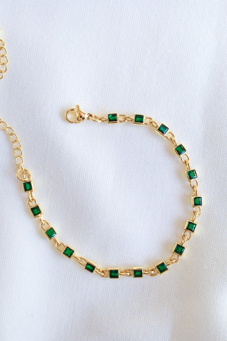 The Paddy Bracelet by Kinsey Designs Archives features green square cubic zirconia stones set in gold-filled metal, shown on a white textured fabric background.