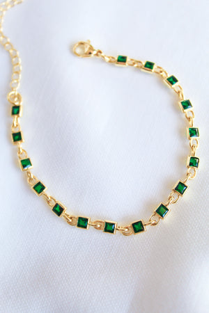 The Paddy Bracelet by Kinsey Designs Archives features square green gemstones and an adjustable gold filled chain, shown on a white fabric background.