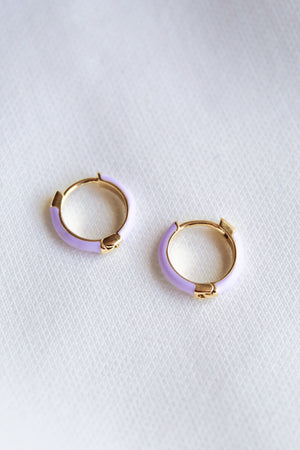 The Pear Huggie - Lavender by Kinsey Designs Archives features gold plated hoop earrings with light purple enamel accents and a 0.5" diameter, shown on a white textured fabric background.
