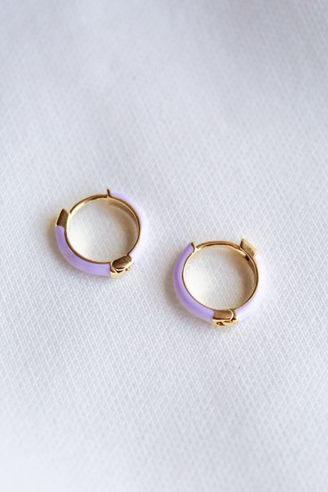 The Pear Huggie - Lavender by Kinsey Designs Archives features gold plated hoop earrings with light purple enamel accents and a 0.5" diameter, shown on a white textured fabric background.