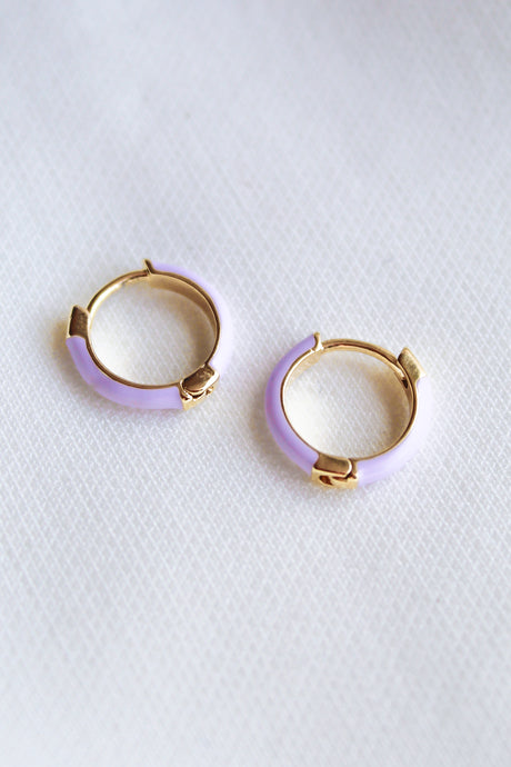 The Pear Huggie - Lavender by Kinsey Designs Archives features two small gold plated hoops with light purple enamel accents, each .5" in diameter, displayed on a white textured surface.