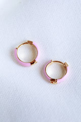 The Kinsey Designs Archives Pear Huggie - Pink features two small gold plated hoop earrings with pastel pink enamel and a .5" diameter, displayed on a white textured fabric background.
