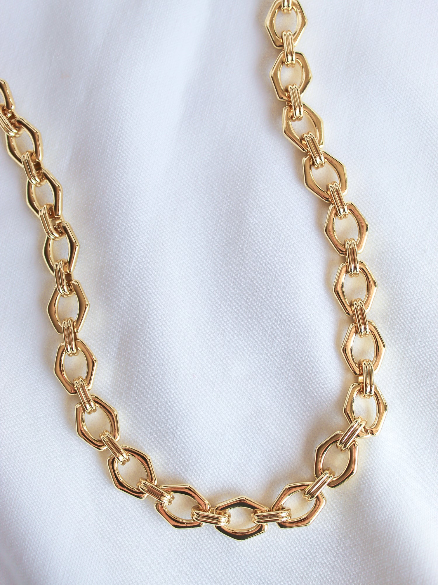 The Prague Necklace by Kinsey Designs Archives features 14k gold filled hexagonal links on an 18" chain, shown on a white fabric background—a modern, elegant accessory for any outfit.