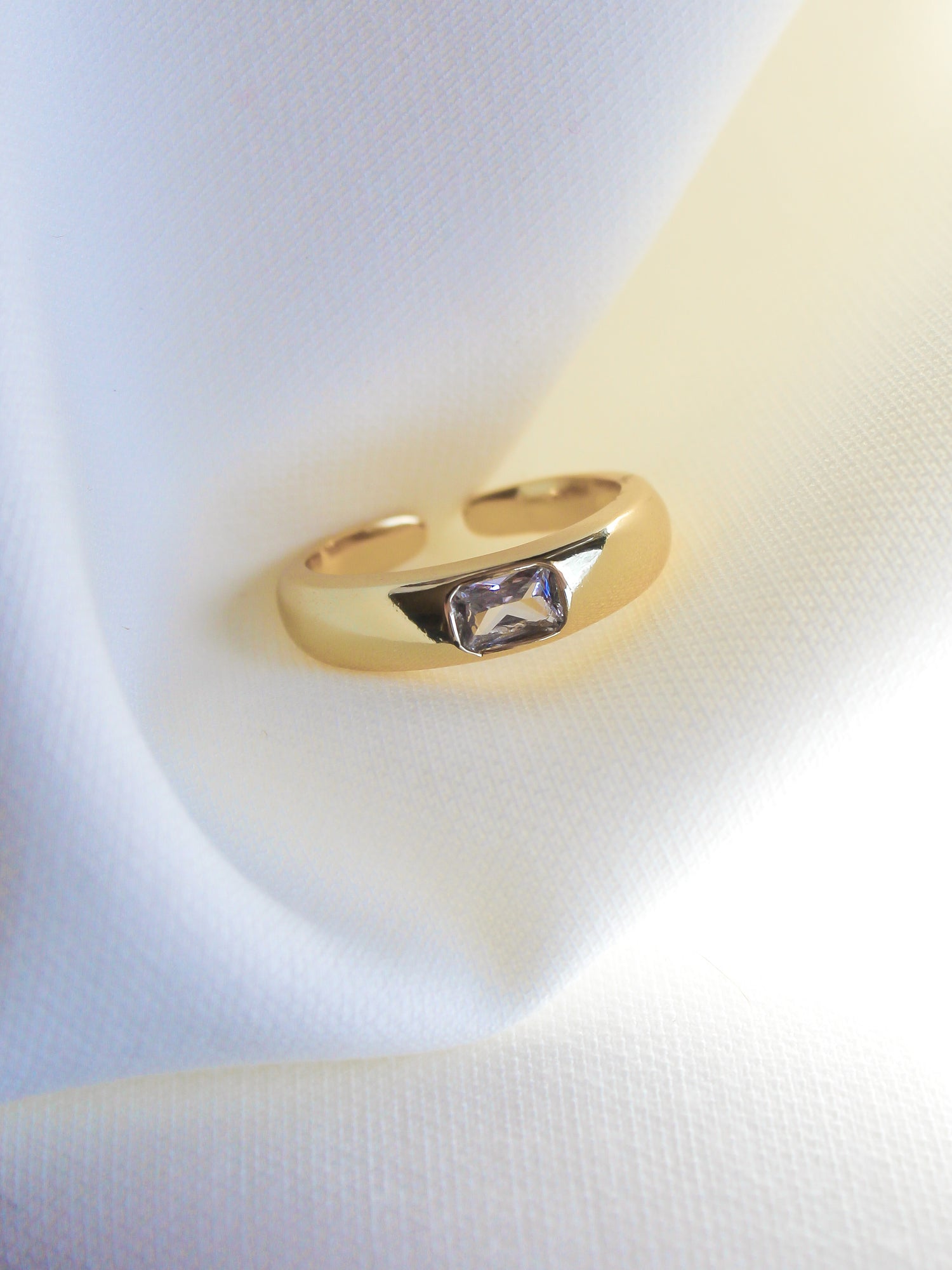 The Preston Ring by Kinsey Designs Archives, featuring a rectangular cubic zirconia and gold plating, is displayed on soft white fabric.