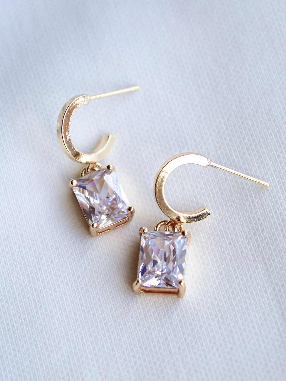 Kinsey Designs Prism Huggies featuring rectangular, princess-cut CZ gemstones, shown on a white fabric background.