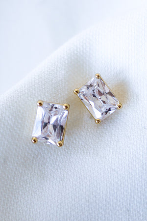 Two rectangular Kinsey Designs Prism Studs with gold prongs rest on white fabric. These elegant Cubic Zirconia earrings offer a modern update to classic style.